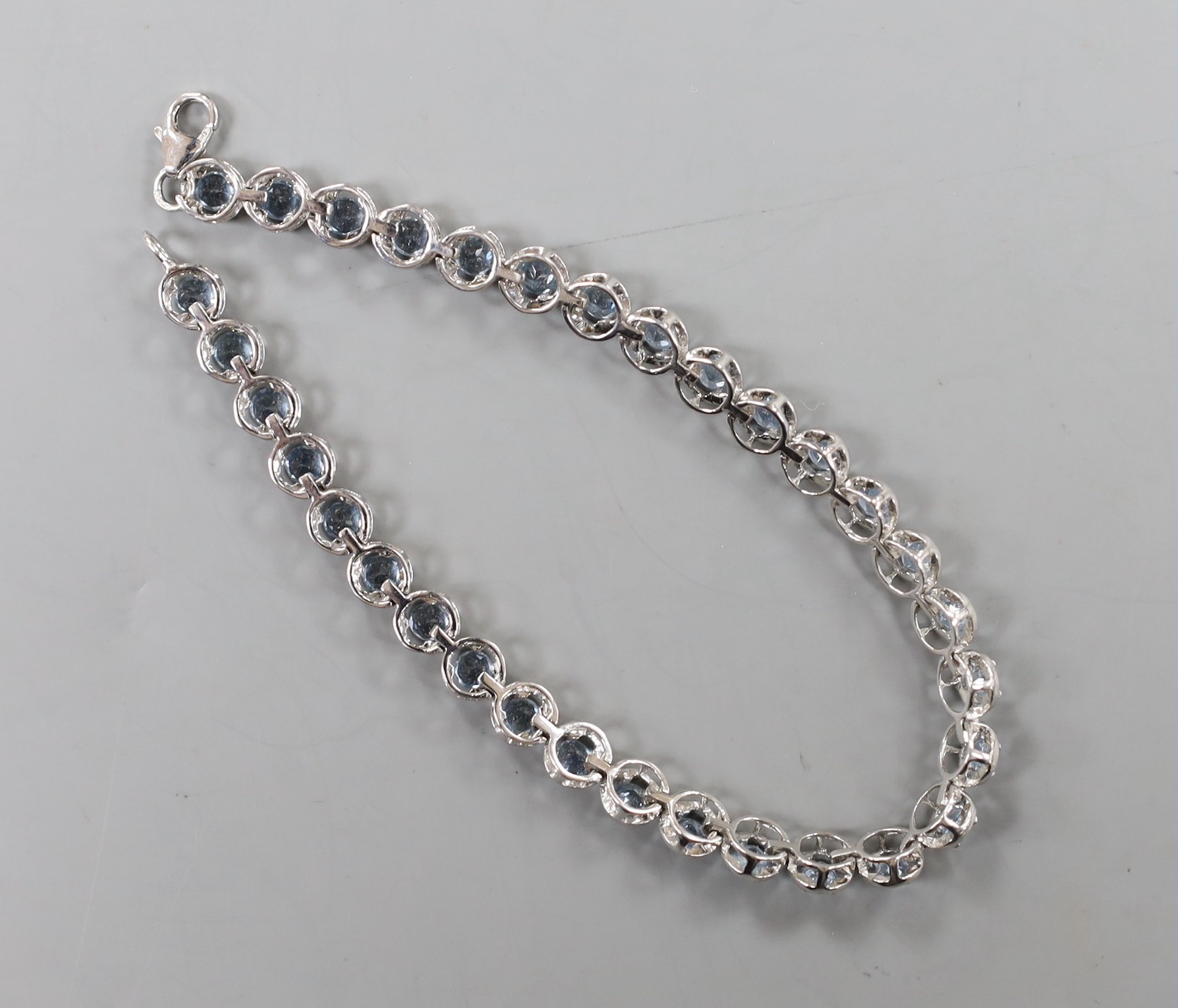 A modern 375 white metal and blue topaz line bracelet, 20cm, set with thirty two stones